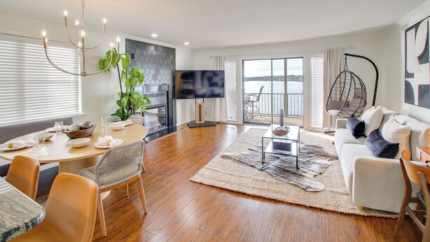 A modern living room with a dining area, a large window with a view, a hanging chair, and a sofa with cushions. - Sunset-view Resort Condo on Lake Hamilton! (Hot Springs)