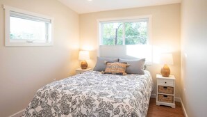 A bedroom with a large bed, two bedside lamps, a window with blinds, and a nightstand with storage baskets. - Golden Cottage Near Red Rocks & School of Mines! (Golden)
