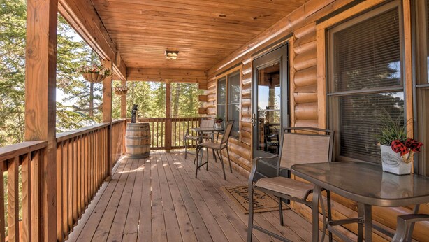 A wooden deck with a railing, a table with chairs, and hanging flower baskets. - Cozy 'nora's Hideaway' - Charming, Quiet Log Cabin (Duck Creek Village)