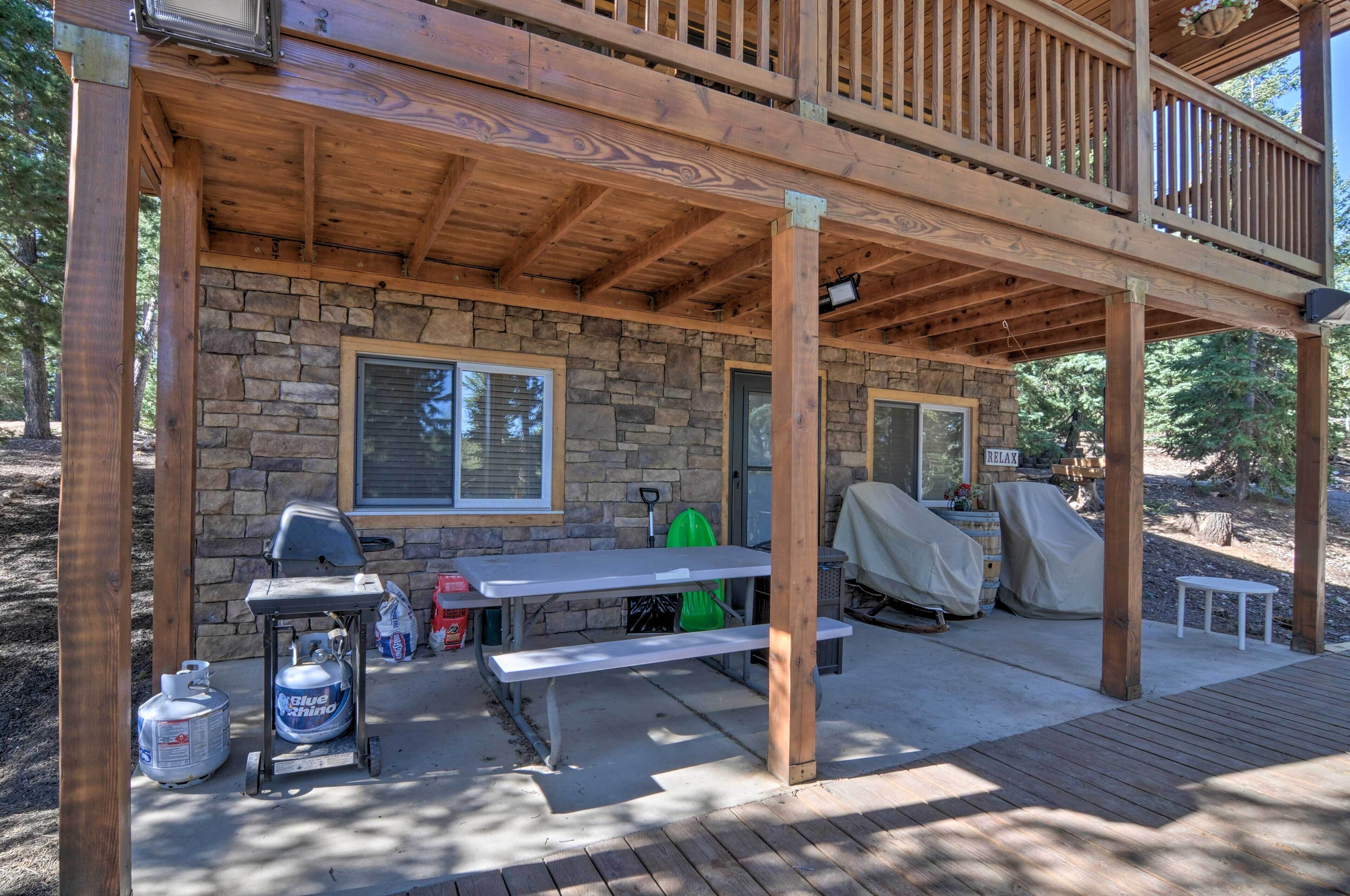 A covered outdoor deck with a stone wall, a grill, a picnic table, and a barbecue grill covered with a canopy.
