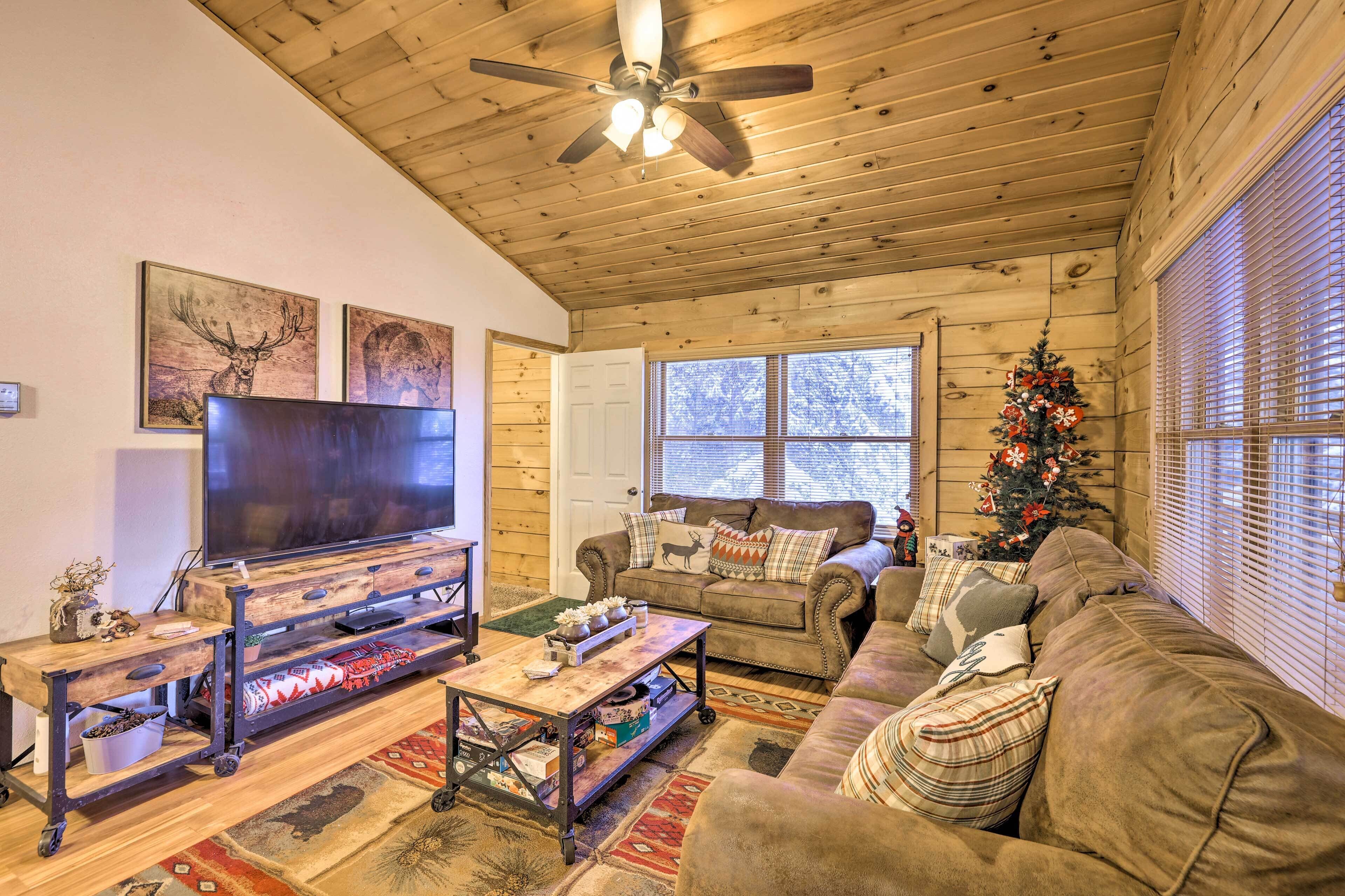 A cozy living room with a wooden ceiling, a large flat-screen TV, a sofa, and a Christmas tree.