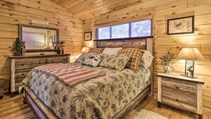 A cozy cabin-style bedroom with a bed, dresser, and window with blinds. - Cozy 'nora's Hideaway' - Charming, Quiet Log Cabin (Duck Creek Village)