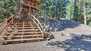 A wooden cabin with a staircase leading to a balcony, surrounded by trees and a gravel path. - Cozy 'nora's Hideaway' - Charming, Quiet Log Cabin (Duck Creek Village)