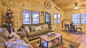 A cozy log cabin interior with a wooden ceiling, a Christmas tree, a sofa with 'joy' and 'deer' pillows, a dining area with a table and chairs, and a fireplace. - Cozy 'nora's Hideaway' - Charming, Quiet Log Cabin (Duck Creek Village)