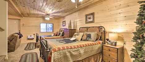 Un dormitorio acogedor con techo de madera, cama con colcha escocesa, mesita de noche con lámpara y un árbol de Navidad.
