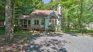 Une petite cabane bleu clair, dotée d’un porche, entourée d’arbres et bordée d’une allée de gravier.