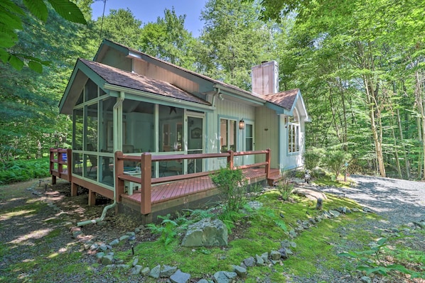 A cabin with a covered porch, surrounded by a forest. - Deck & Resort Amenities: Pocono Lake Home (Pocono Lake)