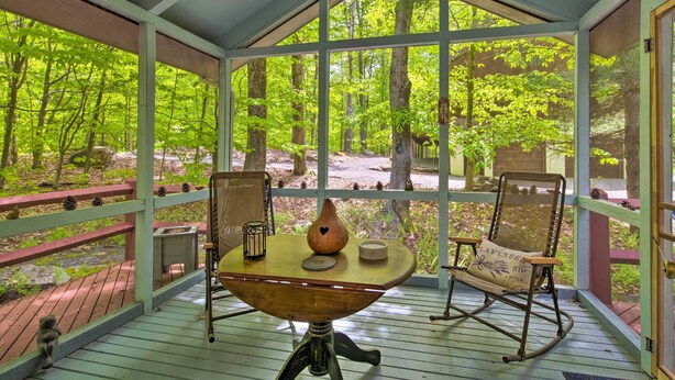 Un espace extérieur abrité, aménagé avec une table, des chaises et offrant une vue sur une forêt.