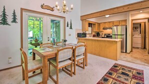 Un coin repas avec une table et des chaises en bois, un lustre et une vue sur la cuisine.