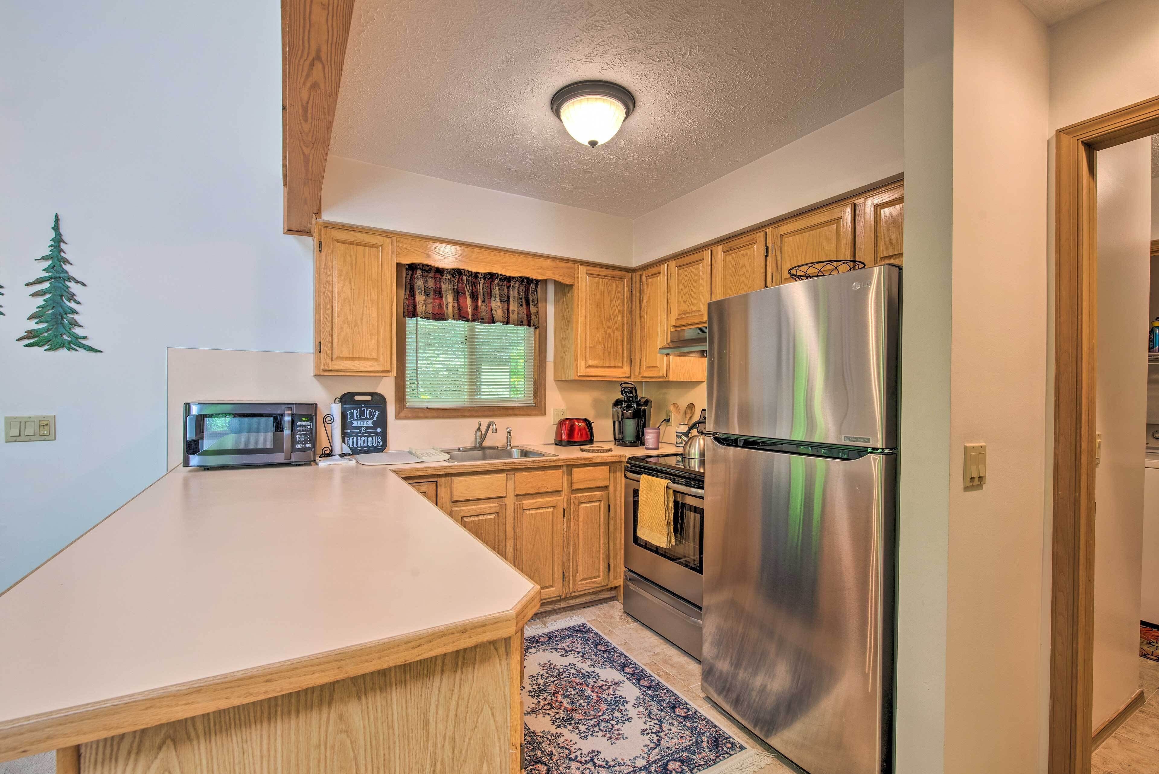 A compact kitchen with wooden cabinets, a stainless steel refrigerator, a microwave, and a coffee maker.