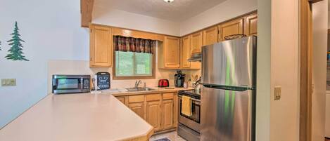 A compact kitchen with wooden cabinets, a stainless steel refrigerator, a microwave, and a coffee maker.