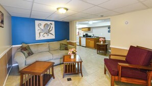 A living room with a sofa, coffee table, and armchair, a kitchen in the background, and a blue accent wall. - Seaside Heights Apt < 2 Blocks to Boardwalk! (Seaside Heights)
