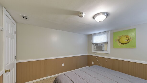 A bedroom with a bed, a door, a window with an air conditioner, and a wall with a painting. - Seaside Heights Apt < 2 Blocks to Boardwalk! (Seaside Heights)