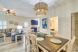 A dining area with a wooden table, white chairs, and a woven pendant light. - Coastal Gulf Shores Getaway - Near the Beaches! (Gulf Shores)