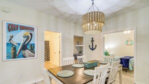 Uma área de refeições com mesa de madeira, cadeiras brancas e luminária pendente.