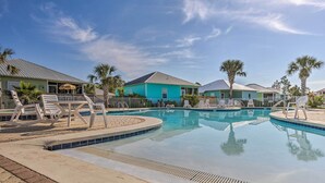 Área de piscina com espreguiçadeiras e um edifício com telhado azul.
