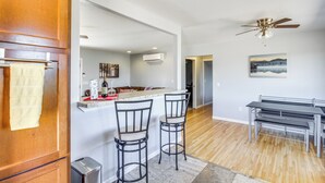 Una cucina moderna con un bancone, due sgabelli da bar, un tavolo da pranzo con sedie, una ventola a soffitto e un quadro appeso al muro.