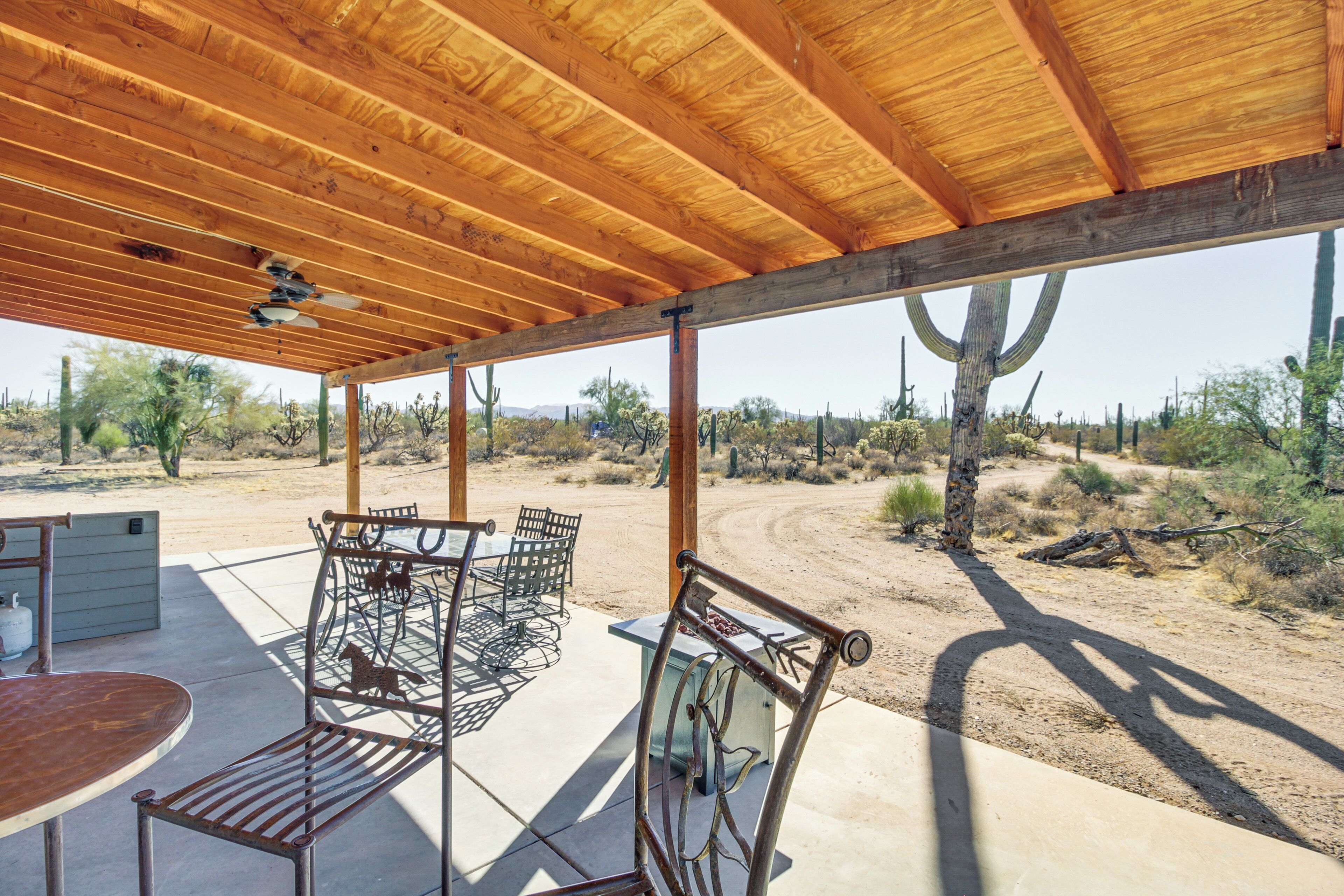 A covered outdoor patio with metal furniture, a table, and a view of a desert landscape.