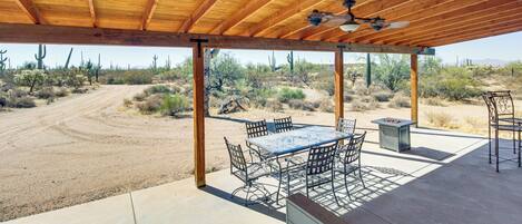 An outdoor patio with a wooden ceiling, a table with chairs, and a view of a desert landscape.
