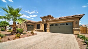 A two-story house with a tiled roof, a garage, and a paved driveway. - Hot Tub & Putting Green: Home in Surprise (Surprise)