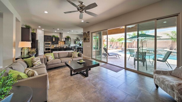 A spacious living area with a large sofa, coffee table, and a ceiling fan. There is a sliding glass door leading to an outdoor patio with a pool and chairs. - Hot Tub & Putting Green: Home in Surprise (Surprise)