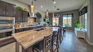 A spacious kitchen with granite countertops, stainless steel appliances, and a large island with bar stools. - Hot Tub & Putting Green: Home in Surprise (Surprise)