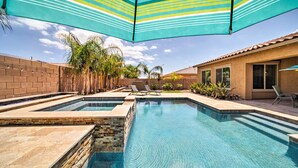 A swimming pool with two separate sections, surrounded by a brick wall and palm trees. - Hot Tub & Putting Green: Home in Surprise (Surprise)