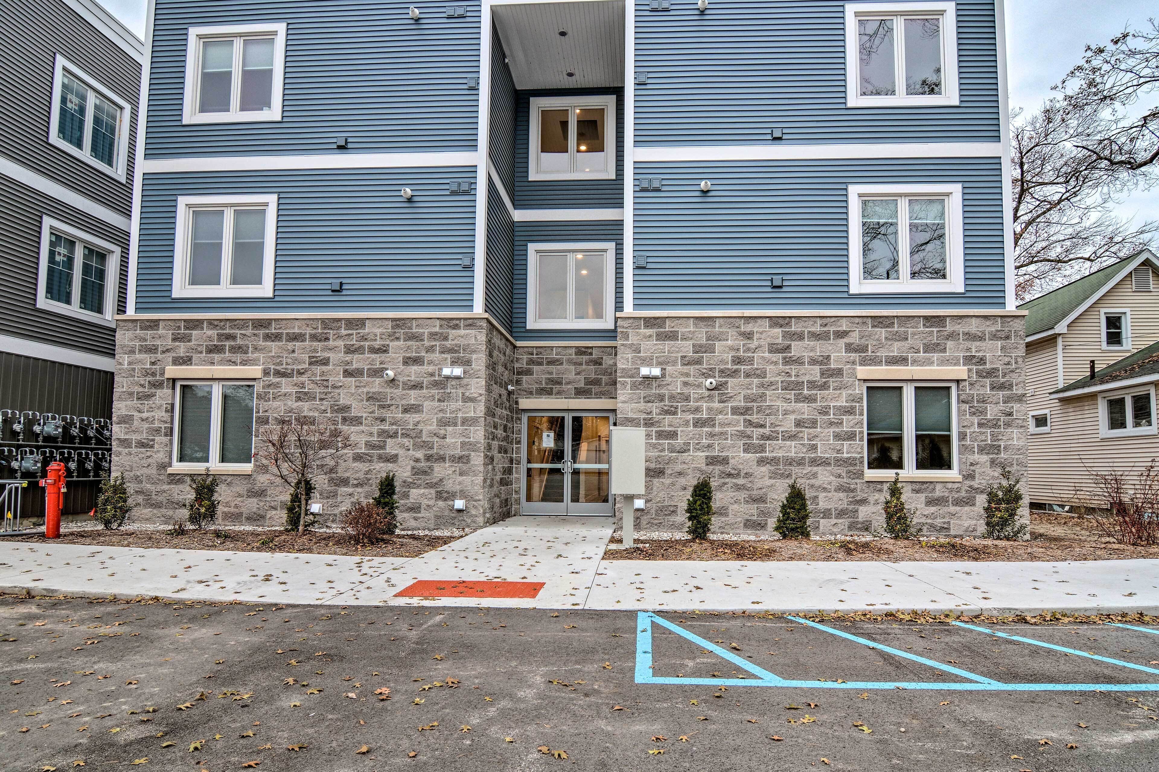 A multi-story building with a stone facade and blue siding, featuring a central entrance with glass doors and a fire hydrant nearby.