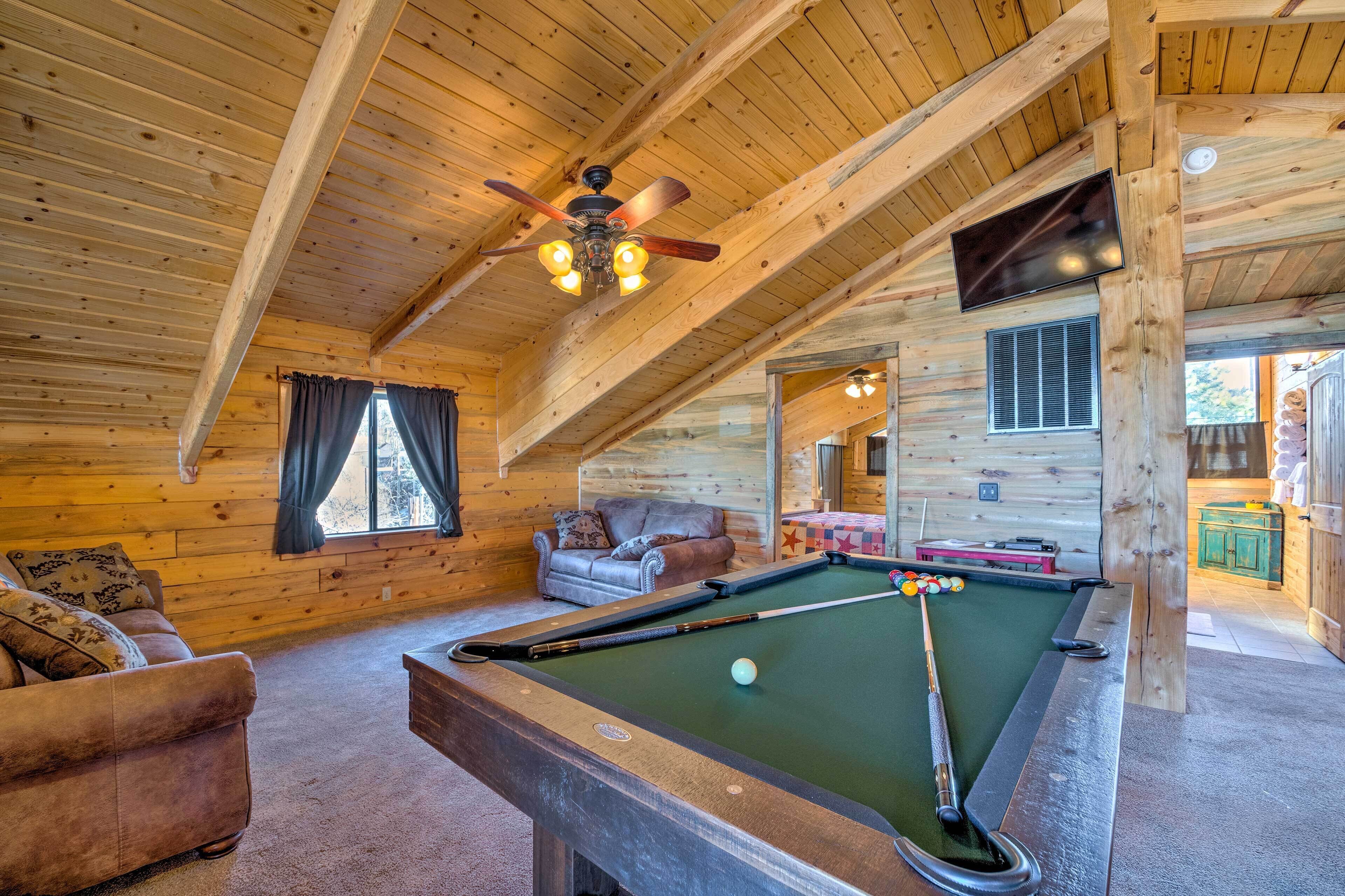 A cozy wooden cabin interior with a pool table, a sofa, and a ceiling fan.