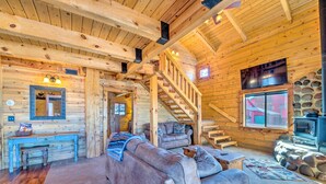 L’intérieur d’une cabane en rondins, avec un escalier, un canapé, une cheminée et un téléviseur.