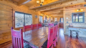 L’intérieur d’un chalet en bois comprend une grande table à manger et des chaises, un coin cuisine et de grandes fenêtres.