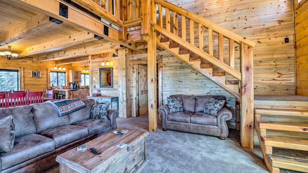 L’intérieur d’une cabane en rondins, avec un escalier en bois, deux canapés, une table basse et un coin cuisine.
