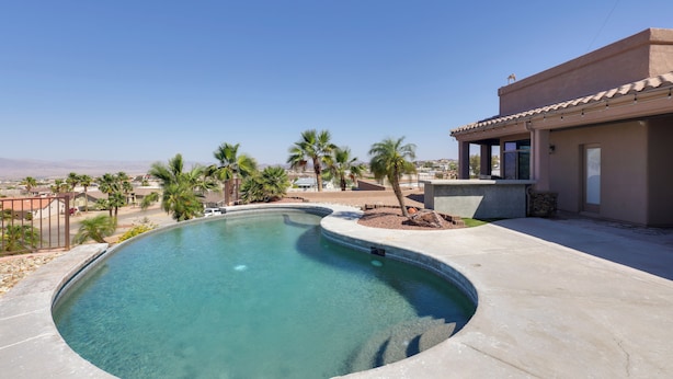 A swimming pool with a curved edge, surrounded by a concrete deck and palm trees. - Infinity Pool & Lake Views: Havasu Group Escape (Lake Havasu City)