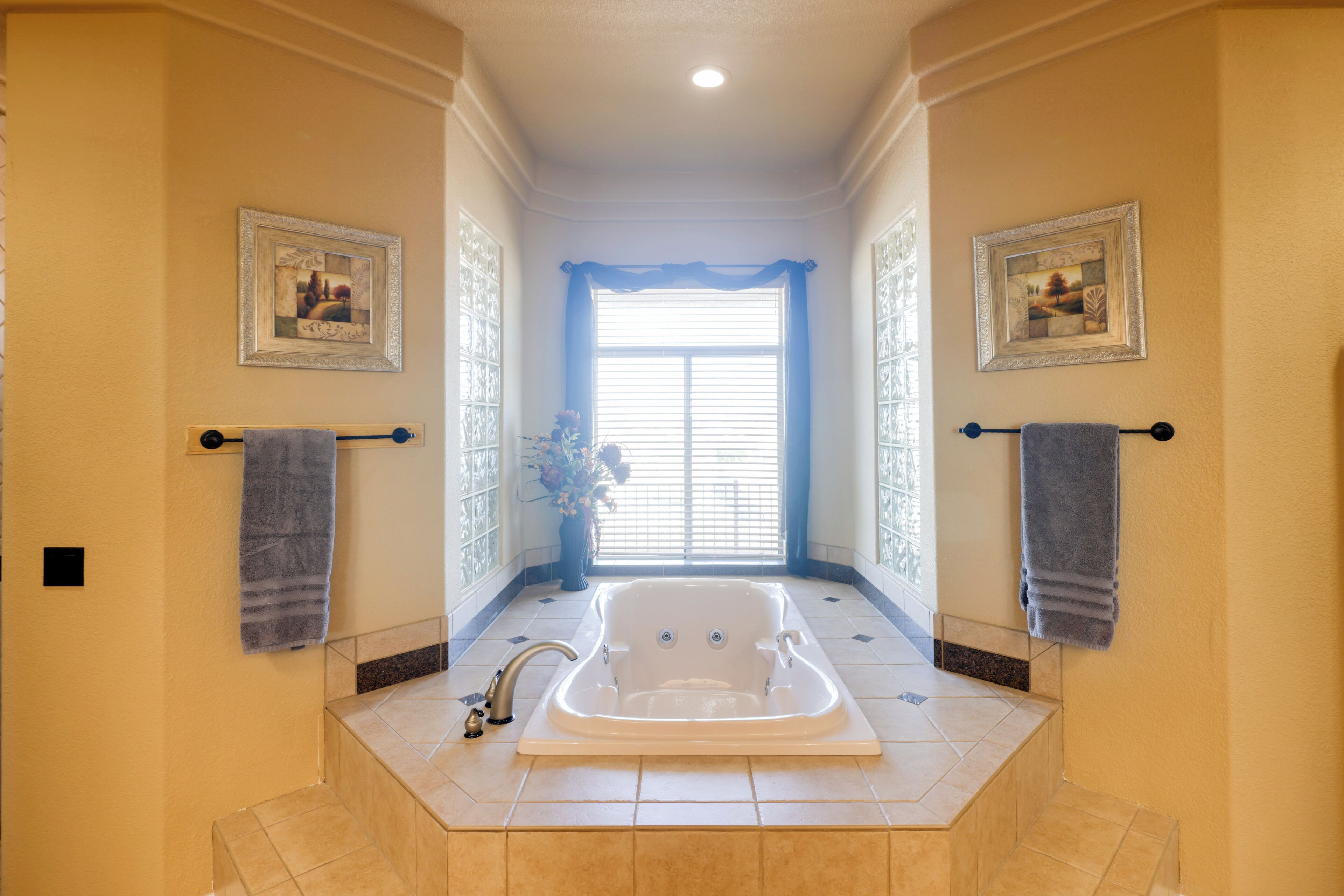 A bathroom with a large bathtub, two towels hanging on towel racks, and a window with curtains.