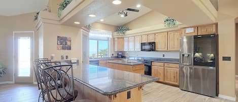 A spacious kitchen with a central island, wooden cabinets, stainless steel appliances, and a view to the outside.
