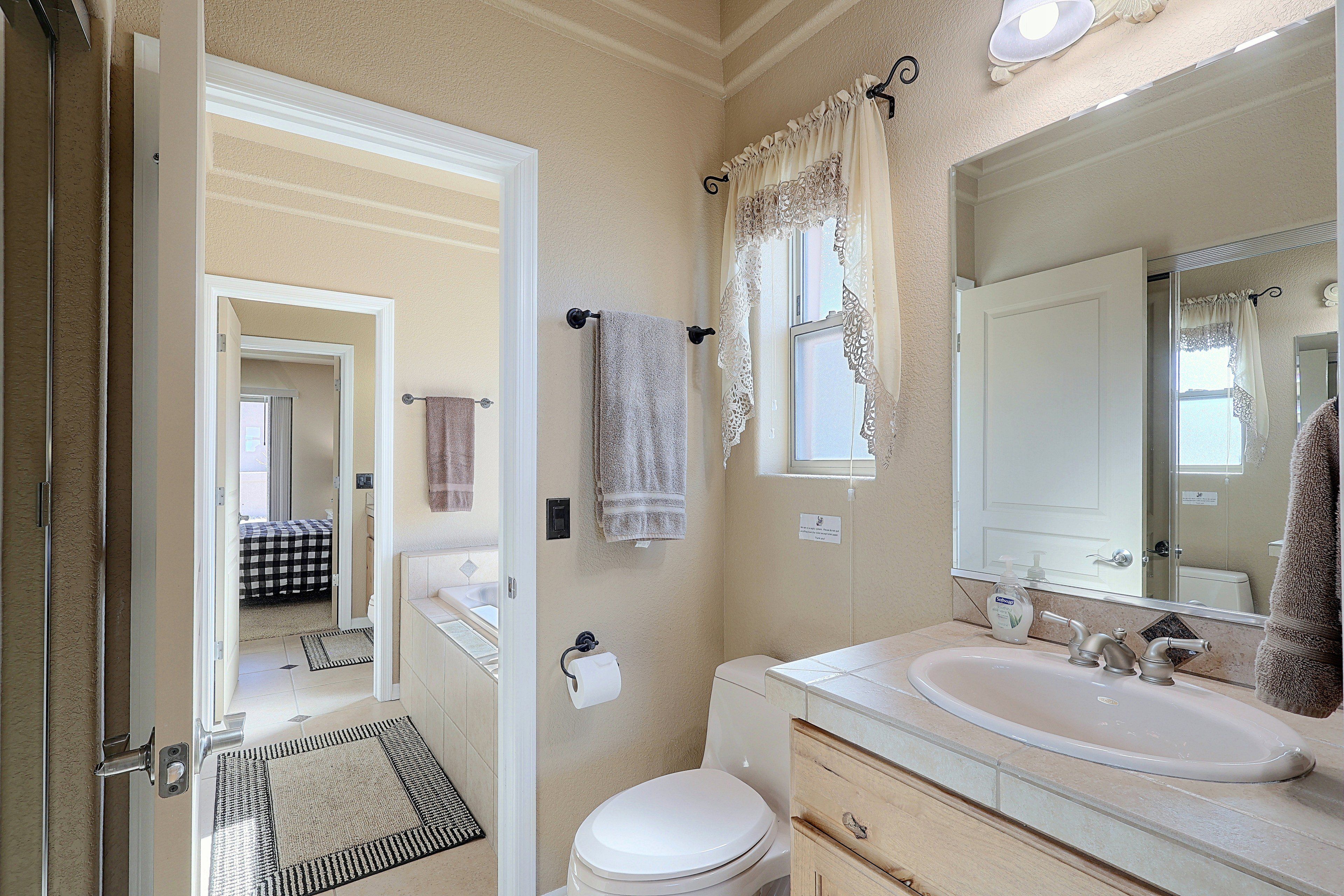 A bathroom with a toilet, sink, and mirror. There is a towel rack with towels and a window with curtains.