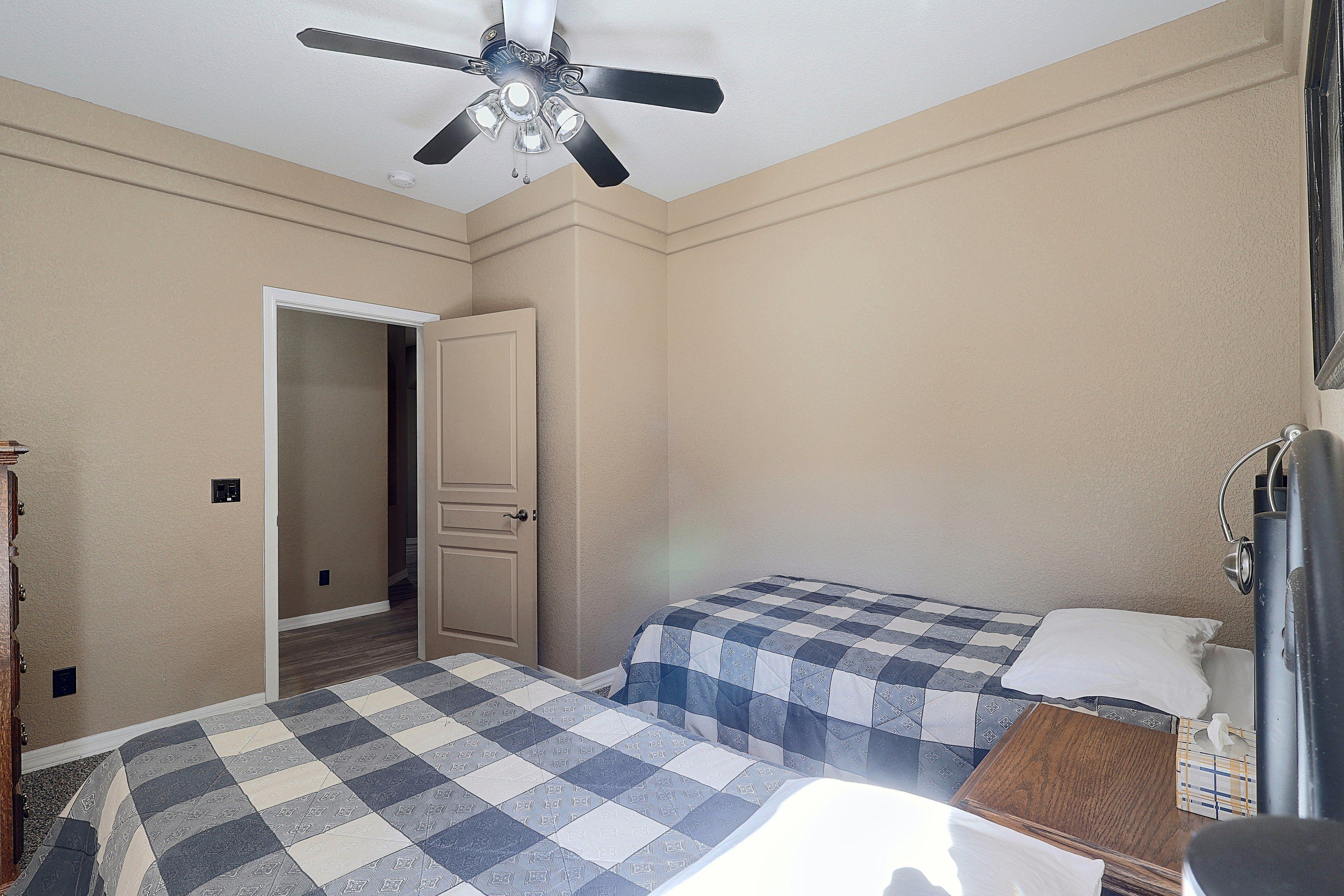 A bedroom with two beds, a ceiling fan, and a door leading to another room.