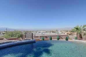 Cielo azul despejado, piscina y vista a un pueblo con montañas al fondo.