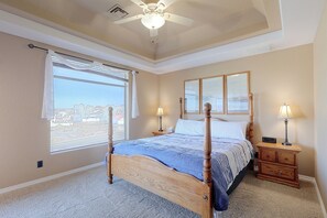 Ein Schlafzimmer mit einem Bett, Nachttischlampen, einem Beistelltisch, einem Fenster mit Blick und einem Deckenventilator.
