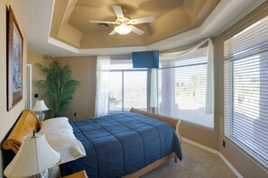 Une chambre à coucher avec un lit, un ventilateur de plafond, une fenêtre avec des stores, une plante et une lampe.