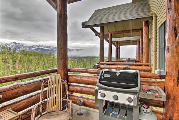 A wooden deck with a grill, chairs, and a view of mountains.