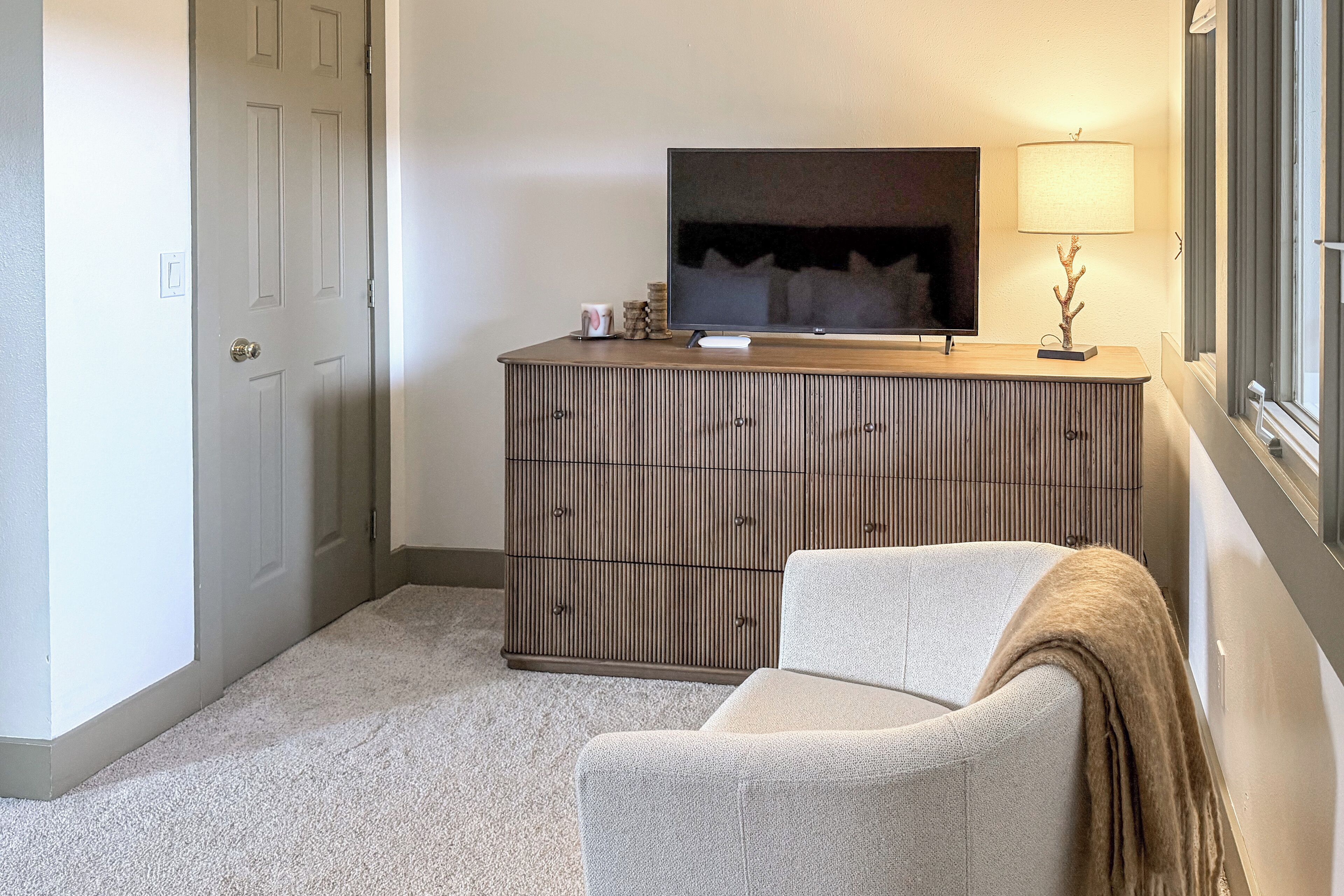 A corner room with a sofa, a cabinet, a television, and a lamp.