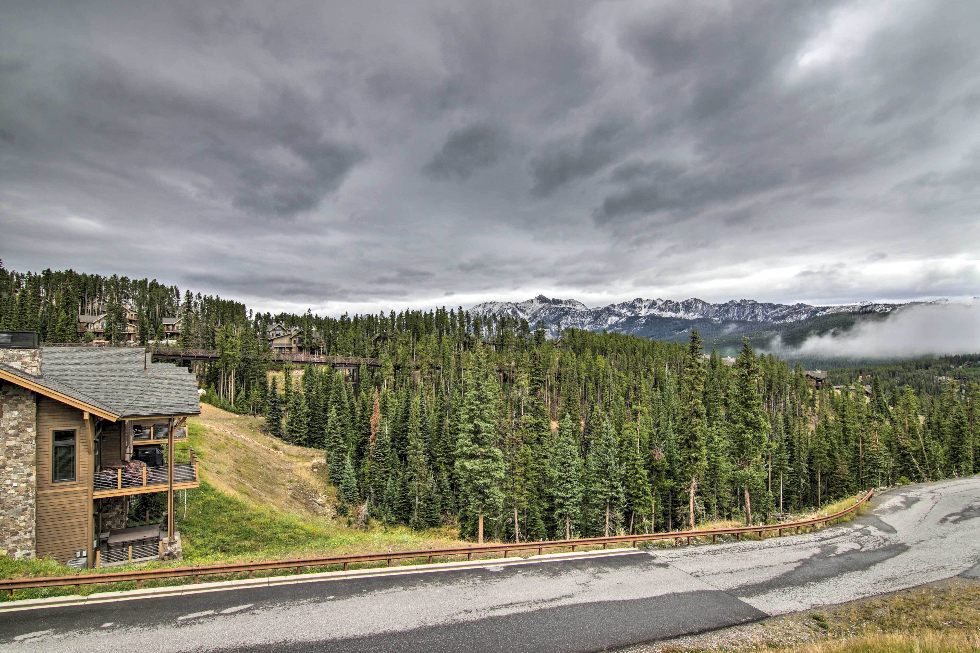 A mountain lodge with a stone exterior, a balcony, and a view of snow-capped mountains.