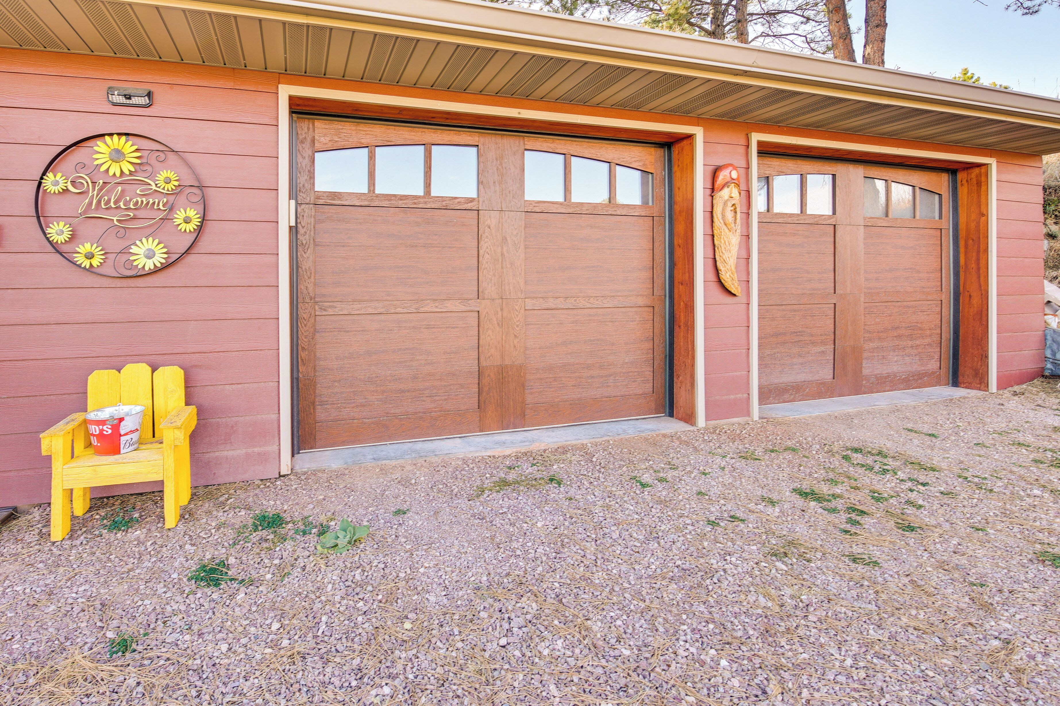 Un bâtiment avec une porte de garage en bois, une pancarte « Bienvenue » ornée de tournesols et une chaise Adirondack jaune avec un seau.