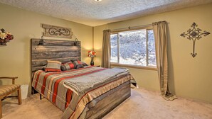 A bedroom with a wooden headboard, a large window with curtains, a bedside lamp, and a decorative wall piece. - Hill City Hideaway Near Mt Rushmore & Hiking (Hill City)