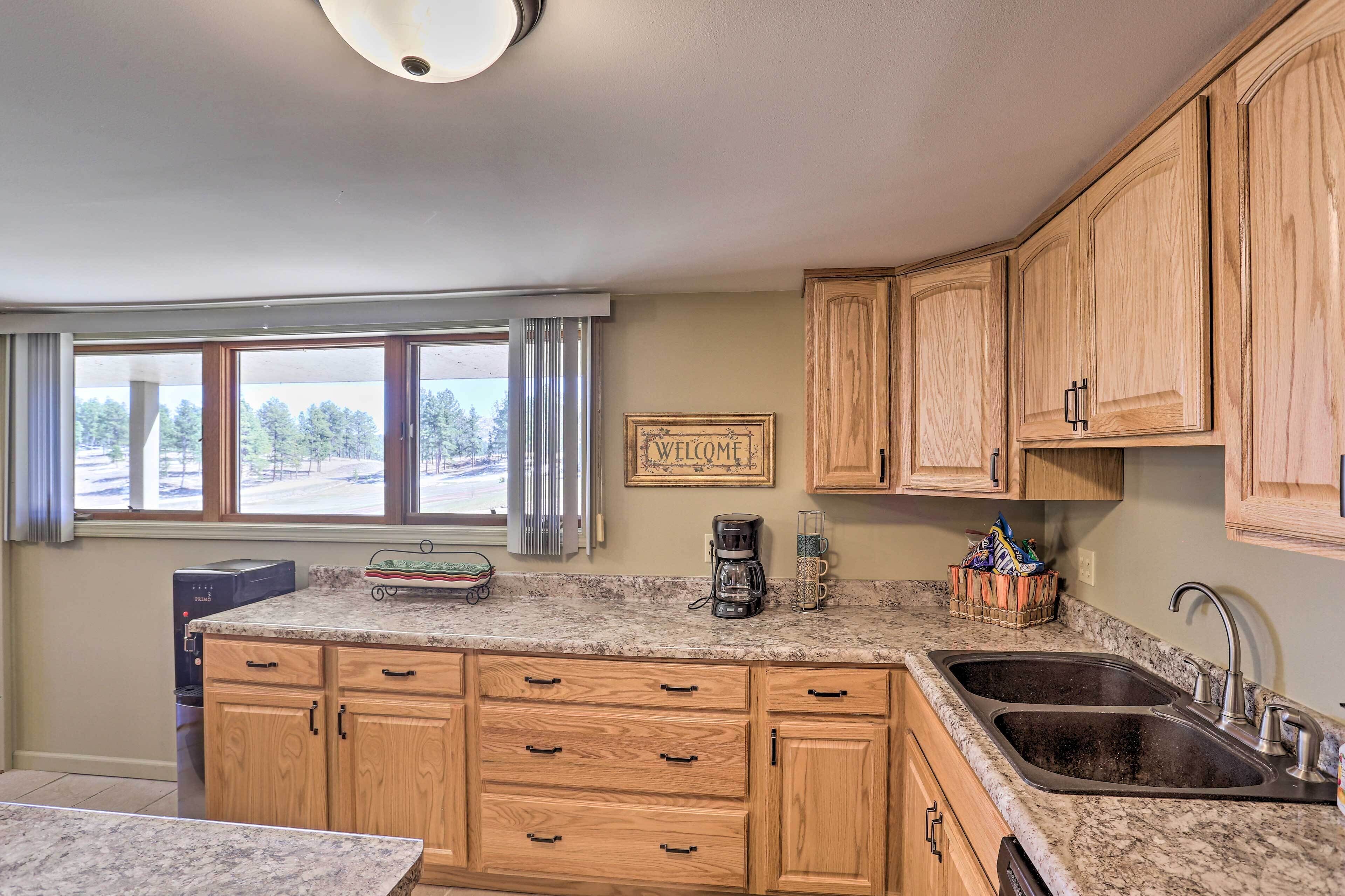 A kitchen with wooden cabinets, a granite countertop, a coffee maker, and a 'Welcome' sign.