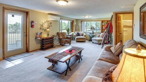 A spacious living room with a large sofa, a coffee table, and a fireplace. There are multiple windows providing natural light and a view of the outdoors. - Hill City Hideaway Near Mt Rushmore & Hiking (Hill City)