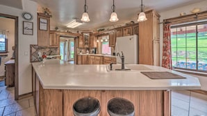 A spacious kitchen with wooden cabinets, a large island, pendant lights, and a view of a garden through the window. - Valley Cloudcroft Hideaway < 8 Mi to Town! (Cloudcroft)