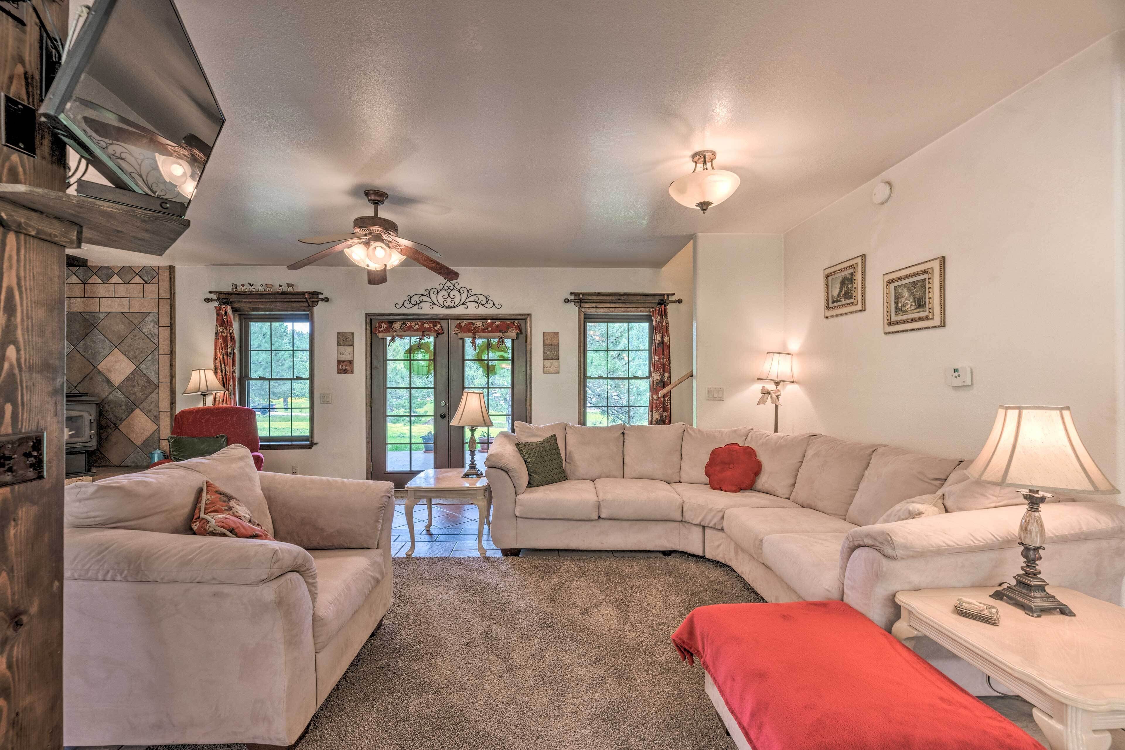 A living room with a fireplace, a ceiling fan, and a large window.
