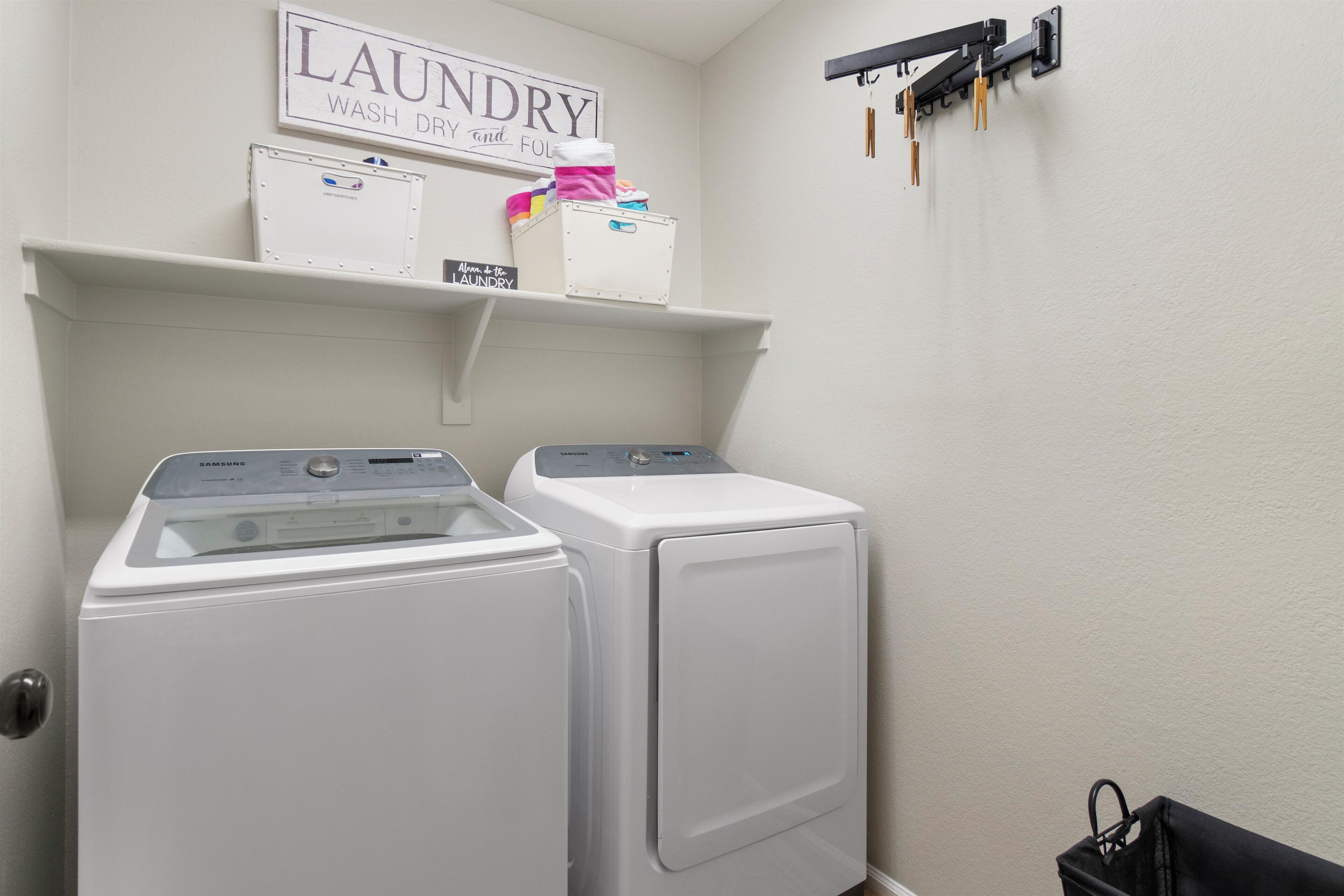 A laundry area with two white washers and dryers, a shelf with laundry supplies, and a sign above the shelf that reads "LAUNDRY WASH DRY and fold".